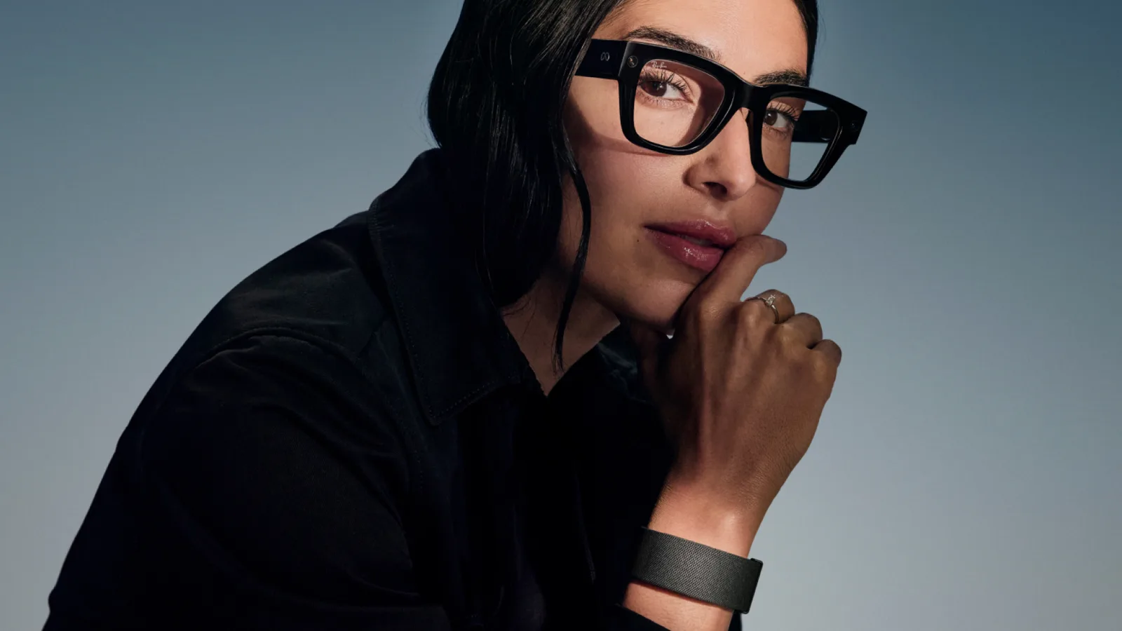 Woman wearing black Meta Ray-Ban Display glasses against a gray background.