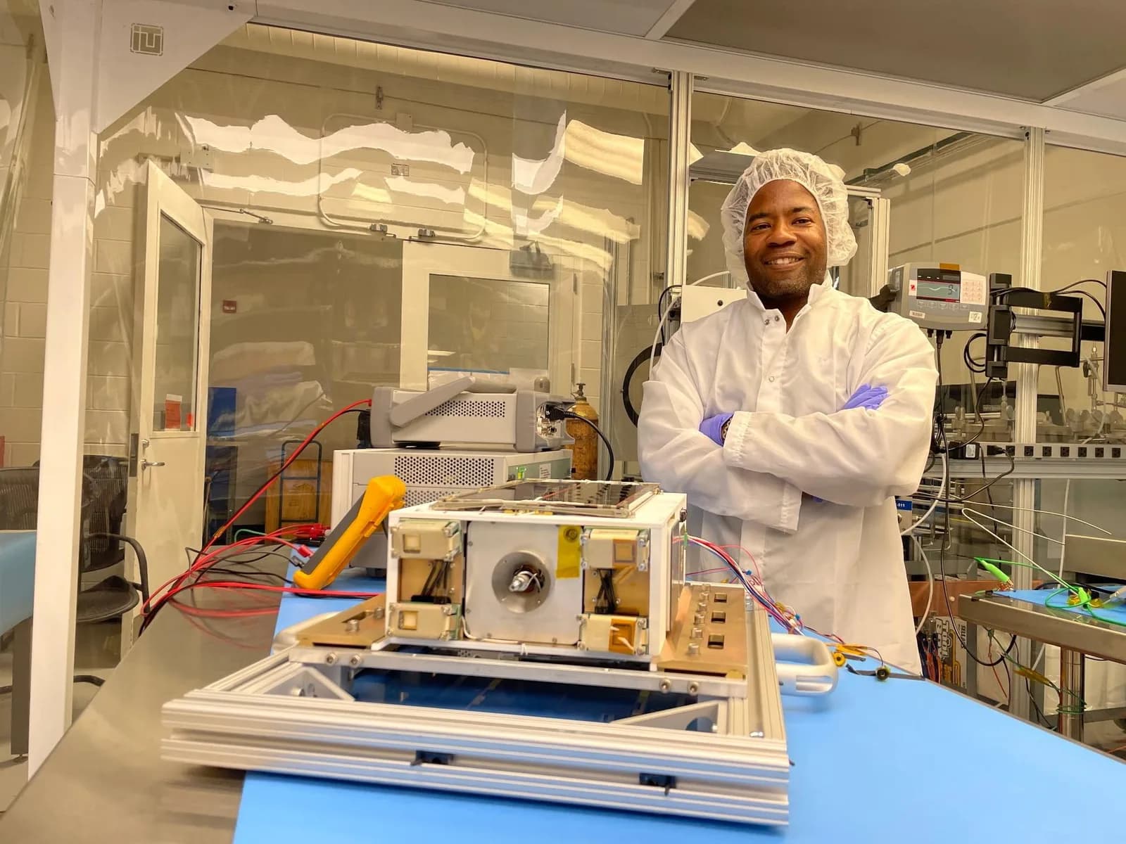 NASA project manager in a clean room beside the small ASCENT dual-mode propulsion spacecraft and test equipment.