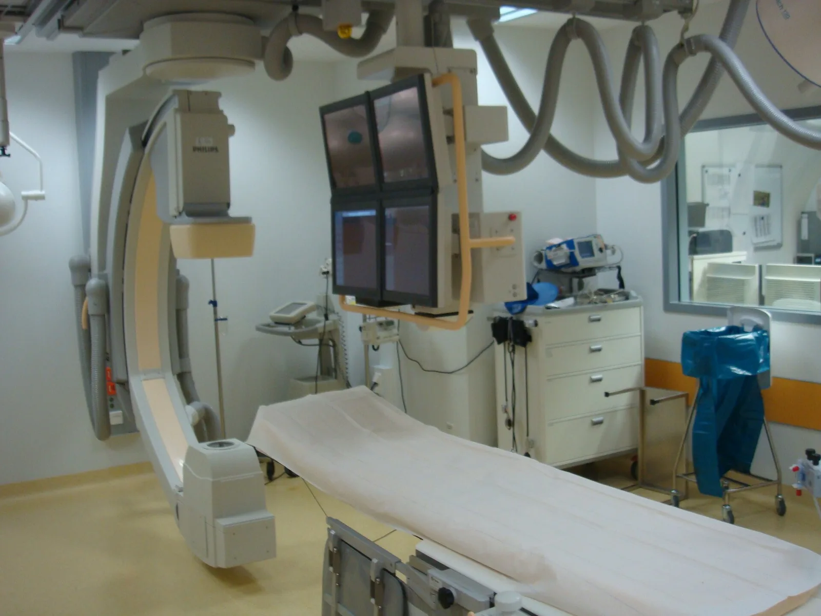 A modern cardiac catheterization laboratory with an X-ray system above the patient table